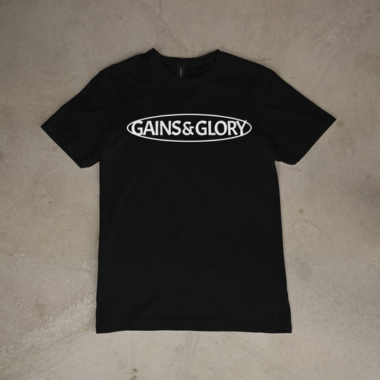 Black t-shirt with 'GAINS & GLORY' text on a concrete floor